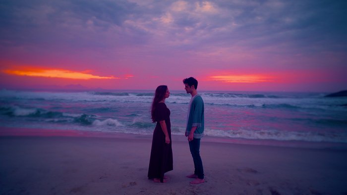 Thumbnail do vídeo: Close-up do casal se olhando na praia com céu magenta em Produção de Videoclipe Conceitual de Lemuriano & Tuca Mei – A Construção da Verdade Cênica | Lampejo Filmes